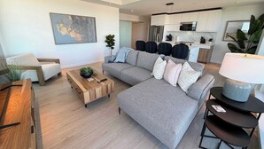 A modern living room with a grey sofa, wooden coffee table, and a dining area with a wooden table. - Waterview 2 BR / 2 Bath penthouse in Northend HFX. (Halifax)