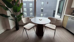 Een moderne keuken met een ronde tafel, twee stoelen, een potplant en een uitzicht op gebouwen door grote ramen.