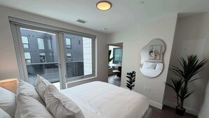 Een moderne slaapkamer met een groot bed, een nachtkastje, een spiegel en een potplant.