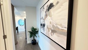A hallway with a large abstract painting, a potted plant, and a circular mirror on the wall. - Downtown Waterview, 2 BR/2 Bath with 6 appliances (Halifax)