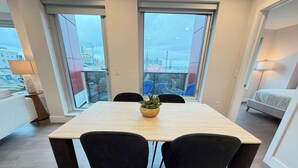 A modern room with a wooden dining table, black chairs, a potted plant, and large windows with a city view. - Downtown Waterview, 2 BR/2 Bath with 6 appliances (Halifax)