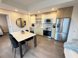 A compact kitchen with a dining table, chairs, a microwave, a refrigerator, and a stove.