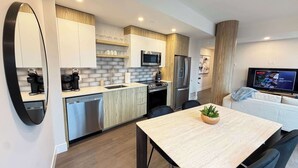 A modern kitchen with a dining area, a TV, and a plant on the table. - Downtown Waterview, 2 BR/2 Bath with 6 appliances (Halifax)