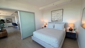 A modern bedroom with a large bed, bedside lamps, a painting, and a sliding door leading to a dining area. - Northend HFX 2 BR/ 2 Bath Penthouse with waterview (Halifax)