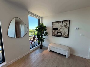 Ein modernes Interieur mit einem großen Fenster, einem runden Spiegel, einer Topfpflanze, einer Bank und einem gerahmten abstrakten Gemälde.
