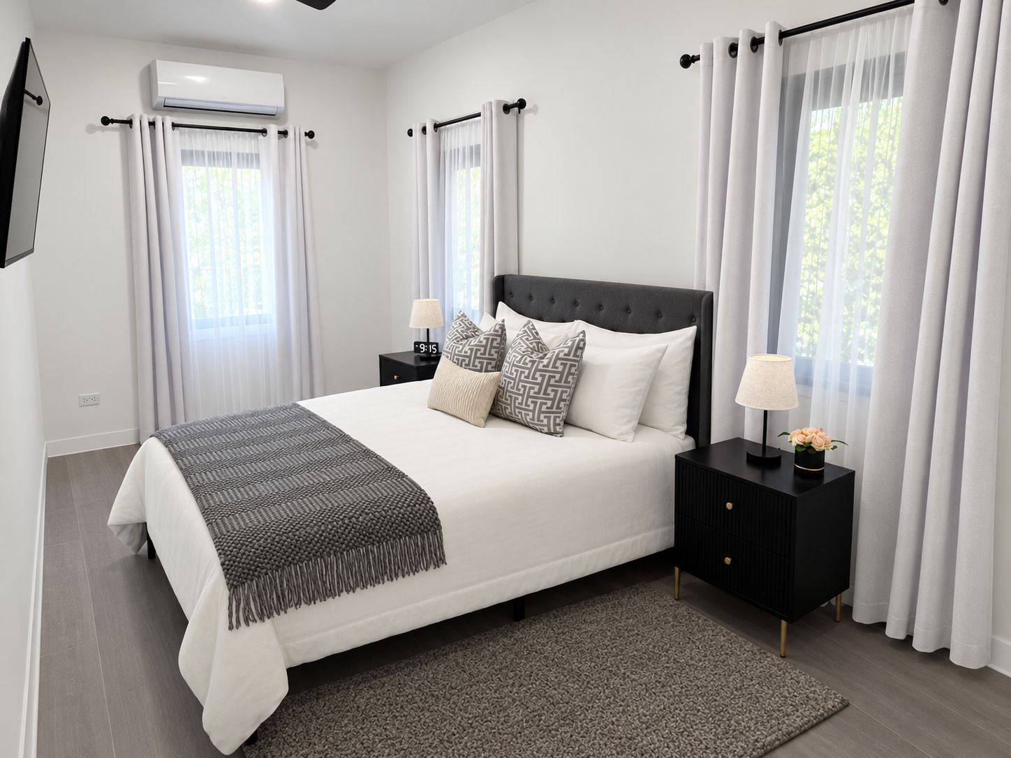 Un dormitorio moderno con una cama grande, dos mesitas de noche, aire acondicionado de pared y cortinas de gasa.
