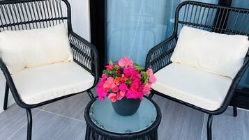Zwei schwarze Korbstühle mit weißen Kissen und ein Glastisch mit einem Blumentopf.