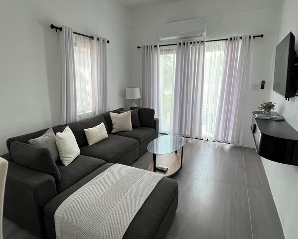 Ein modernes Wohnzimmer mit einer Couch, einem Glastisch und einem an der Wand befestigten Fernseher.