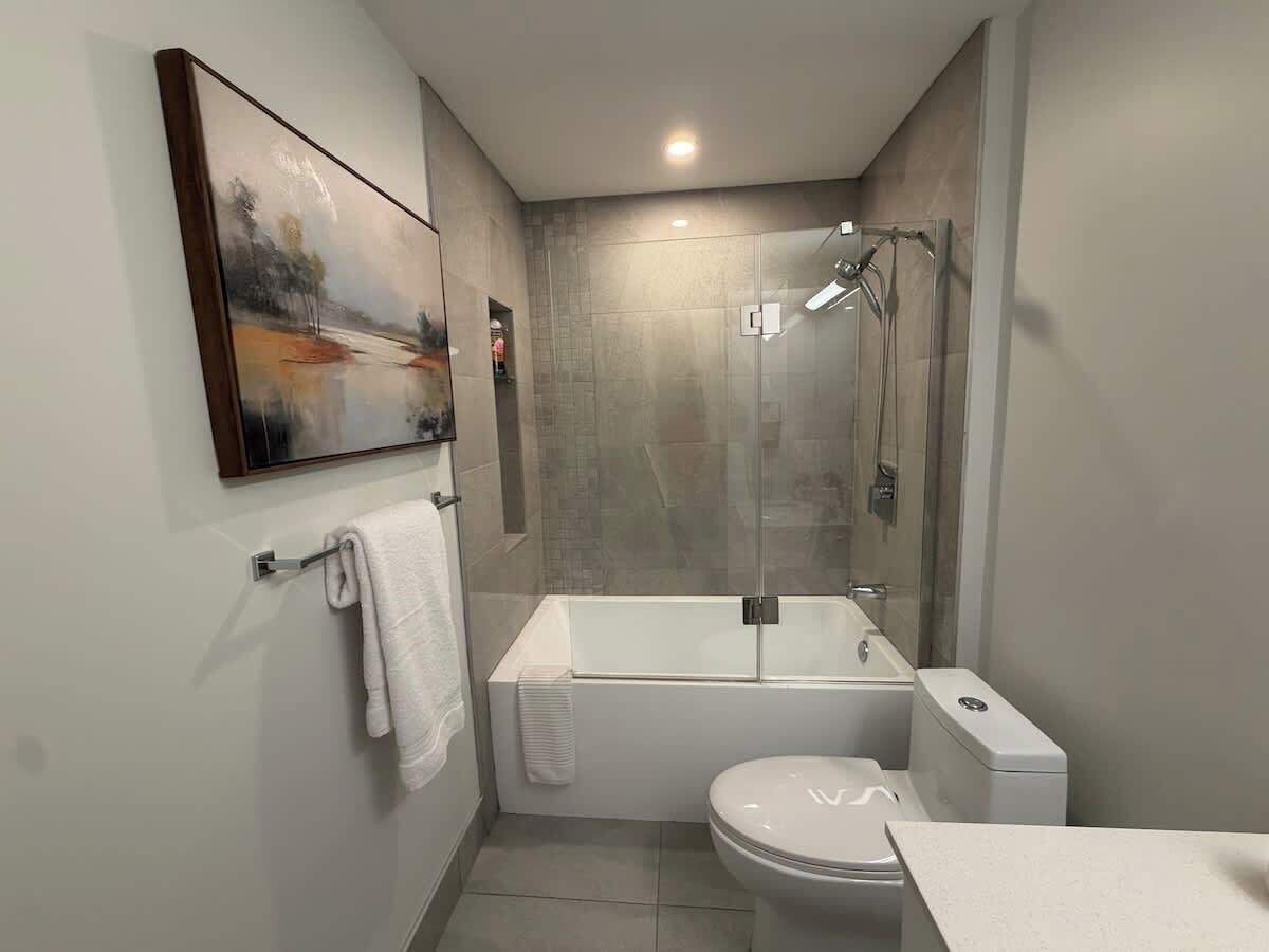 A modern bathroom with a bathtub, toilet, and glass-enclosed shower.