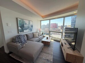 A modern living room with a sofa, coffee table, and TV stand, large windows with a city view. - 2 BR & 2 Bath luxury condo with amazing city views! (Halifax)