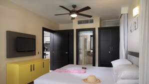 A hotel room with a bed, a television, a ceiling fan, a yellow cabinet, and a bathroom visible through a glass door. - Presidential suite  2 bedrooms and pool view in Lifestyle Cabarete (Cabarete)