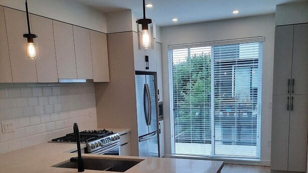 Uma cozinha moderna com uma ilha central, eletrodomésticos de aço inoxidável e uma janela grande com persianas.