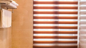 A bathroom with a tiled wall, a towel rack with folded towels, and a window with blinds. - Metra Tower (Phnom Penh)