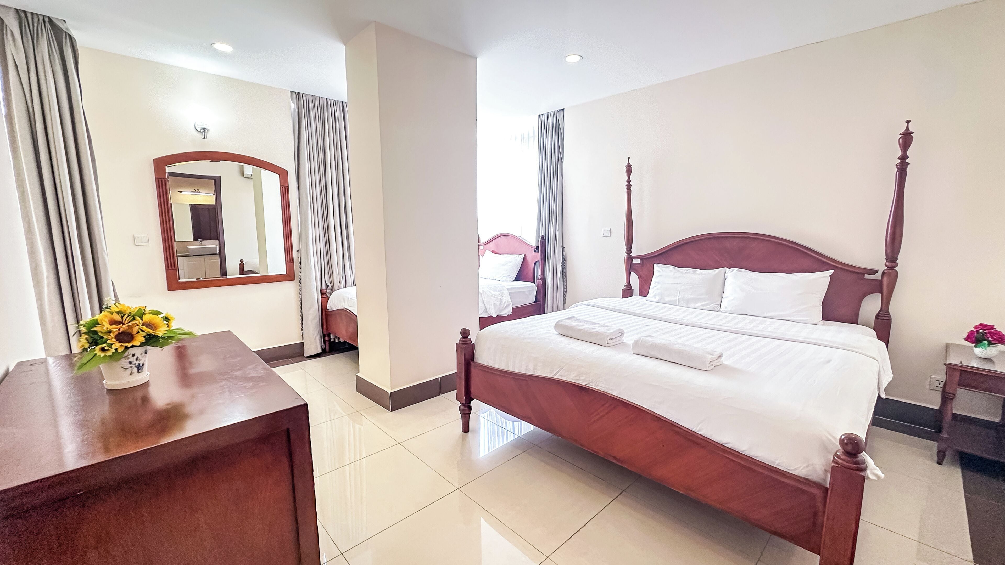 Una habitación de hotel con una cama grande, un escritorio de madera, un espejo y un jarrón con flores.