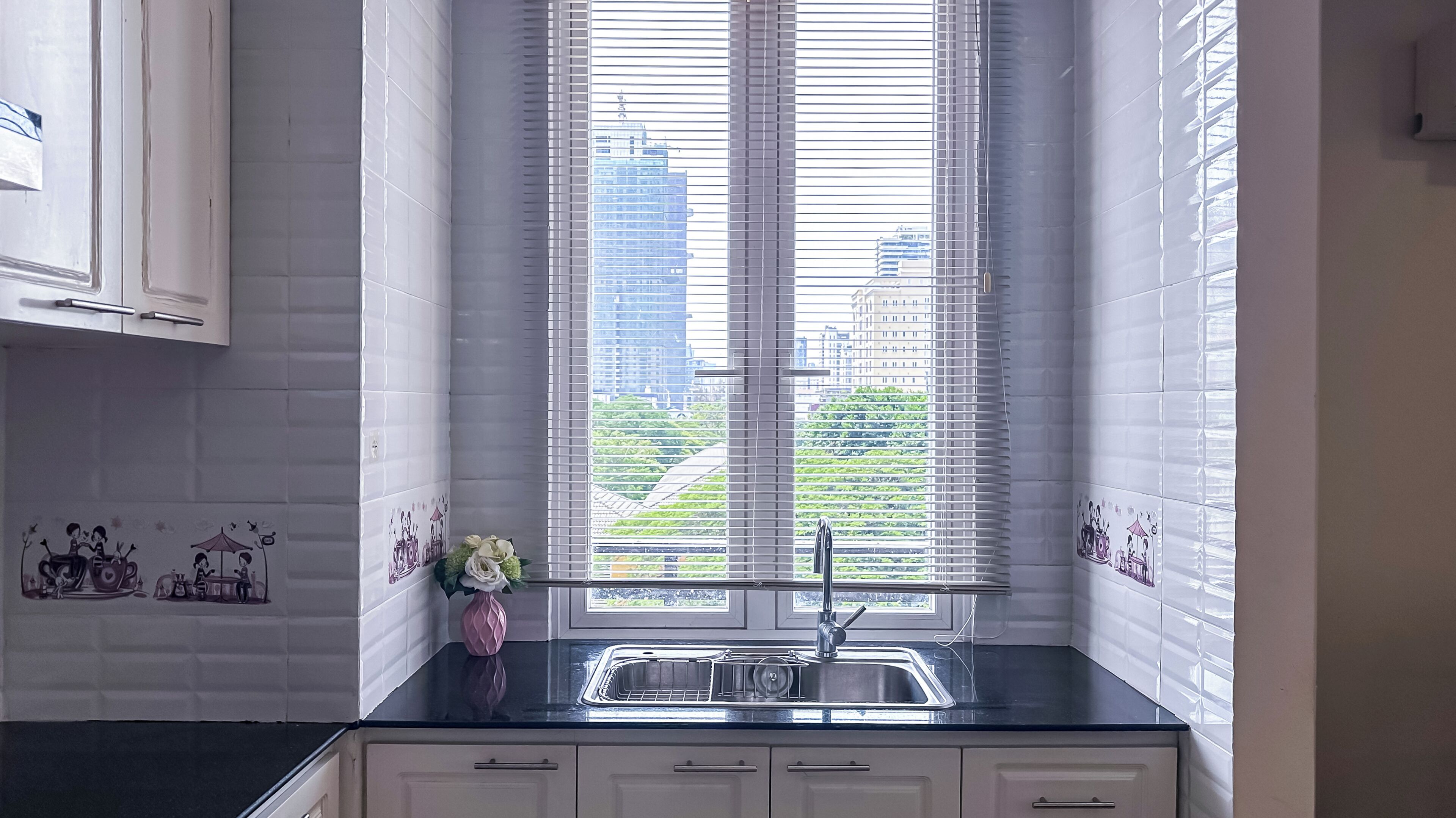 A kitchen with a window, white cabinets, and a black countertop.