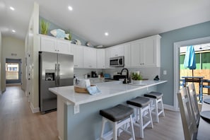 A modern kitchen with white cabinets, a stainless steel refrigerator, a microwave, and a large island with bar stools. - Green door cottage 3-bedroom house in charming St. Augustine (St. Augustine)
