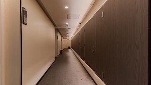A long, narrow hallway with a carpeted floor, wooden panel walls, and recessed lighting.