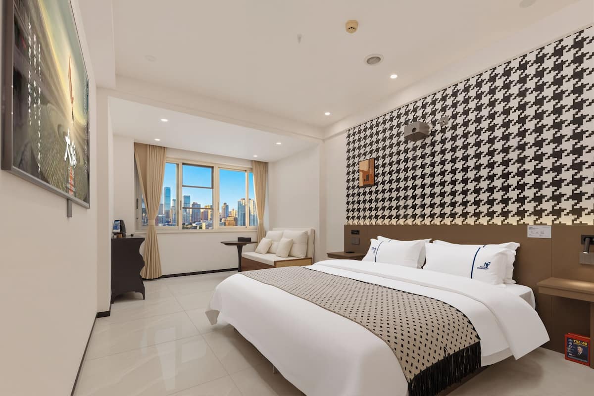 Ein Hotelzimmer mit einem großen Bett, Blick auf die Stadt, einer Wand mit Hounds-Tooth-Muster und einem Empfangsbereich.