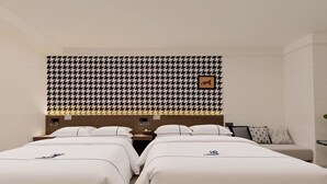 A hotel room with two beds, a houndstooth patterned headboard, a framed picture, and a bedside table with a lamp.