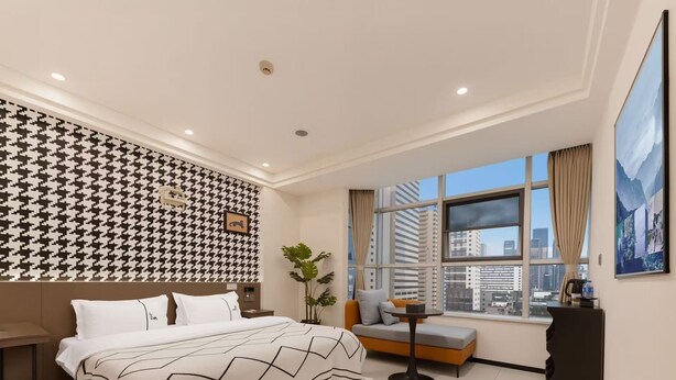 A modern hotel room with a large bed, a sofa, a small table, and a window with a city view.