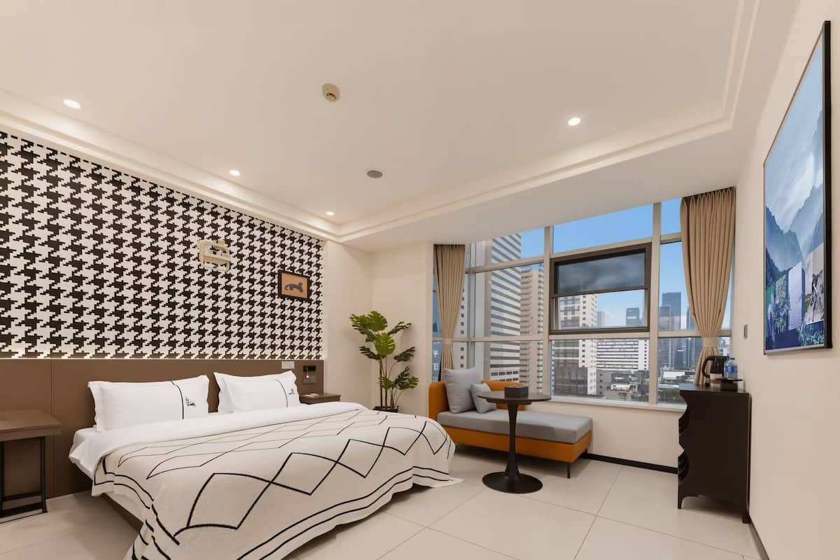 Ein modernes Hotelzimmer mit einem großen Bett, einer Couch, einem kleinen Tisch und einem Fenster mit Blick auf die Stadt.