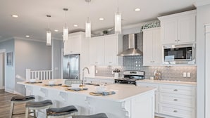 A modern kitchen with white cabinetry, a central island, stainless steel appliances, and pendant lighting. - All BEACH! 2nd row w/full views, Sleeps 16, FUN! (Bolivar Peninsula)