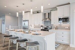 A modern kitchen with white cabinetry, a central island, stainless steel appliances, and pendant lighting. - All BEACH! 2nd row w/full views, Sleeps 16, FUN! (Bolivar Peninsula)