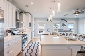 A modern kitchen with white cabinetry, a central island, pendant lights, and a ceiling fan. - All BEACH! 2nd row w/full views, Sleeps 16, FUN! (Bolivar Peninsula)