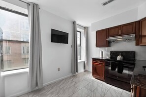 Una cocina con televisor, armarios de madera, estufa y ventana con cortinas.