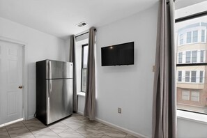 Una cocina compacta con un refrigerador de acero inoxidable, un televisor de pantalla plana montado en la pared y un ventanal con cortinas.