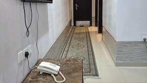 A hallway with a marble-tiled floor, a patterned rug, a mounted TV, and a telephone on a table.