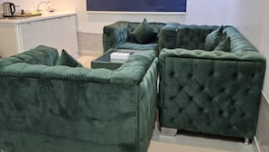 A green upholstered sectional sofa with a tufted design, a coffee table, and a built-in kitchen area with a sink and countertop.