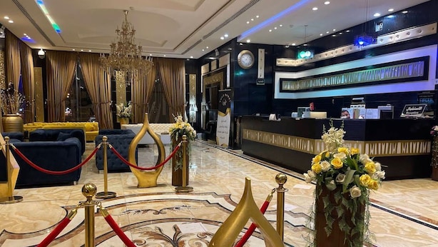 A hotel lobby with a reception desk, red velvet ropes, and a chandelier.