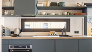 Uma cozinha moderna com forno embutido, janela sobre a pia e prateleira com louças e utensílios.