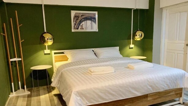 Ein Bett mit weißer Bettwäsche, zwei Nachttische, eine grüne Wand und ein gerahmtes Bild über dem Bett.
