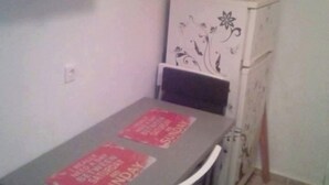 A small dining area with a table and chairs, a refrigerator with decorative patterns, and a wall-mounted shelf above the table. - Cozy 2-bedroom Center in Thessaloniki (Thessaloniki)