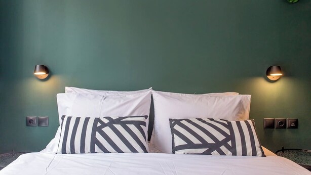 A bed with white bedding and black and white striped pillows, two wall-mounted light fixtures, and a green wall. - Cozy 2-bedroom Center in Thessaloniki (Thessaloniki)