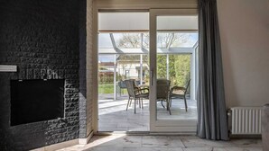 Habitació amb paret de pedra, porta corredissa de vidre que dona a un pati exterior amb cadires i taula, i un radiador al sòl.
