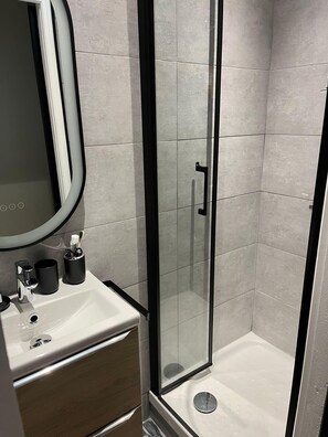 Ein modernes Badezimmer mit Duschkabine aus Glas, einem Waschbecken mit Spiegel und einer Toilette.