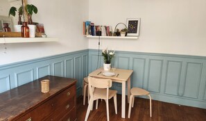 Ein Essbereich mit Winkelcouch, einem Holztisch und Stühlen, einer Topfpflanze und einem Bücherregal mit Büchern und Dekoration.