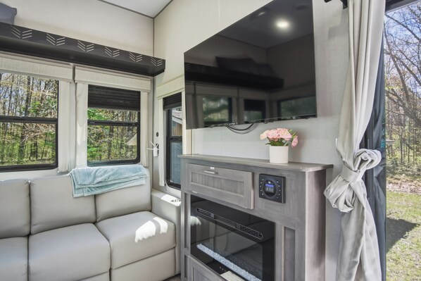 Un intérieur de camping-car compact comprenant un coin cuisine, un espace salon et une fenêtre donnant sur la forêt.
