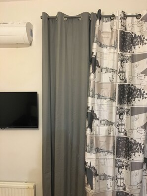Ein Badezimmer mit grauer Duschvorhang, einem an der Wand montierten Flachbildfernseher und einem weißen Heizkörper.