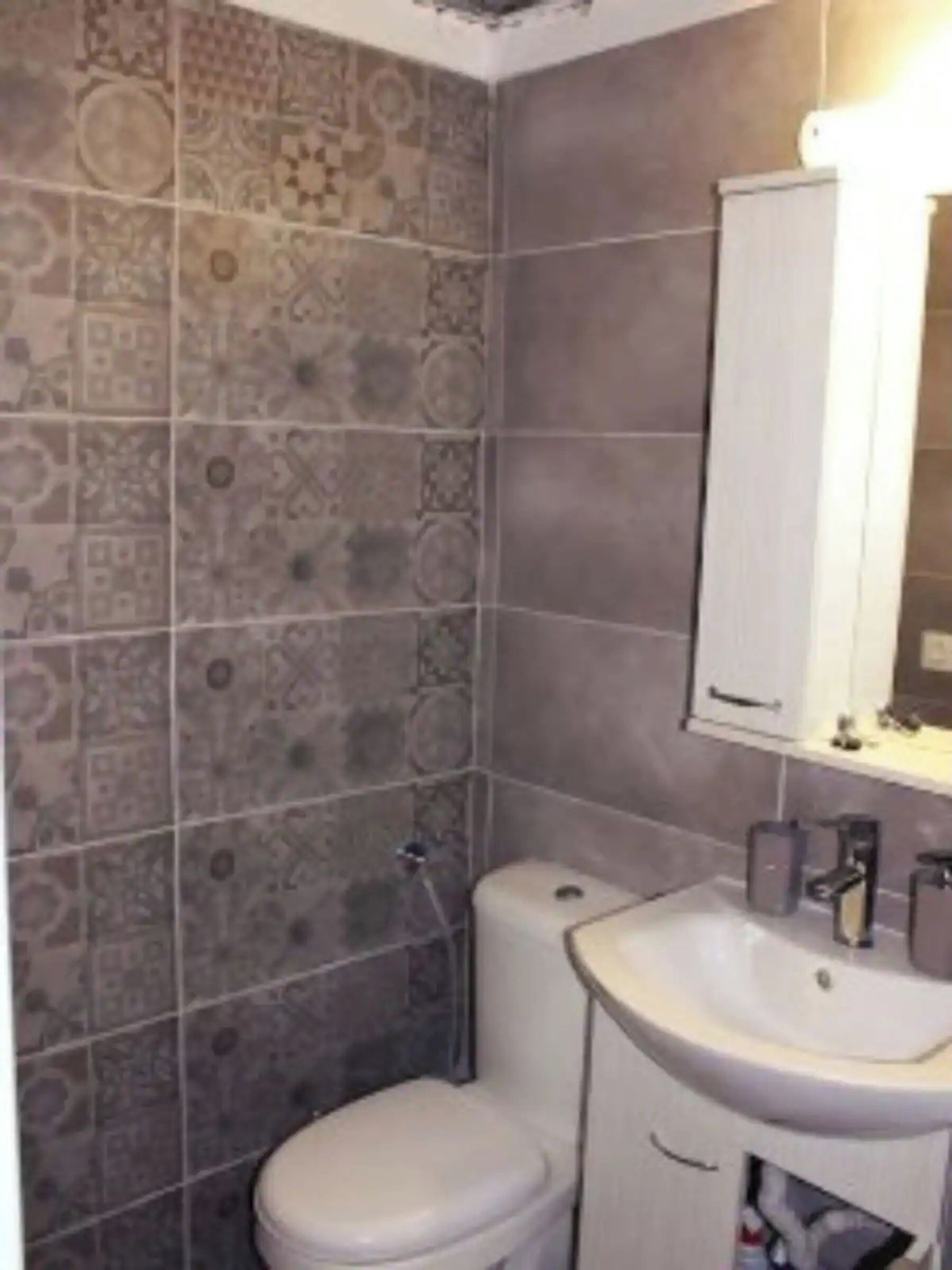 A bathroom with patterned tiles, a white toilet, a sink, and a mirror.