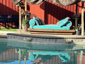 Eine Poolliege mit blauer Couch, Blumentöpfen und einem roten Gebäude im Hintergrund.