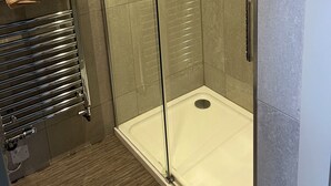 Eine Dusche mit Glasabtrennung, ein weißer Boden, ein chromfarbener Handtuchhalter mit Handtuch und geflieste Wände.