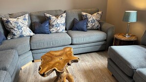 Ein graues Sofa mit Kissen in floralem Muster, ein Holztisch und eine Lampe auf einem Beistelltisch.