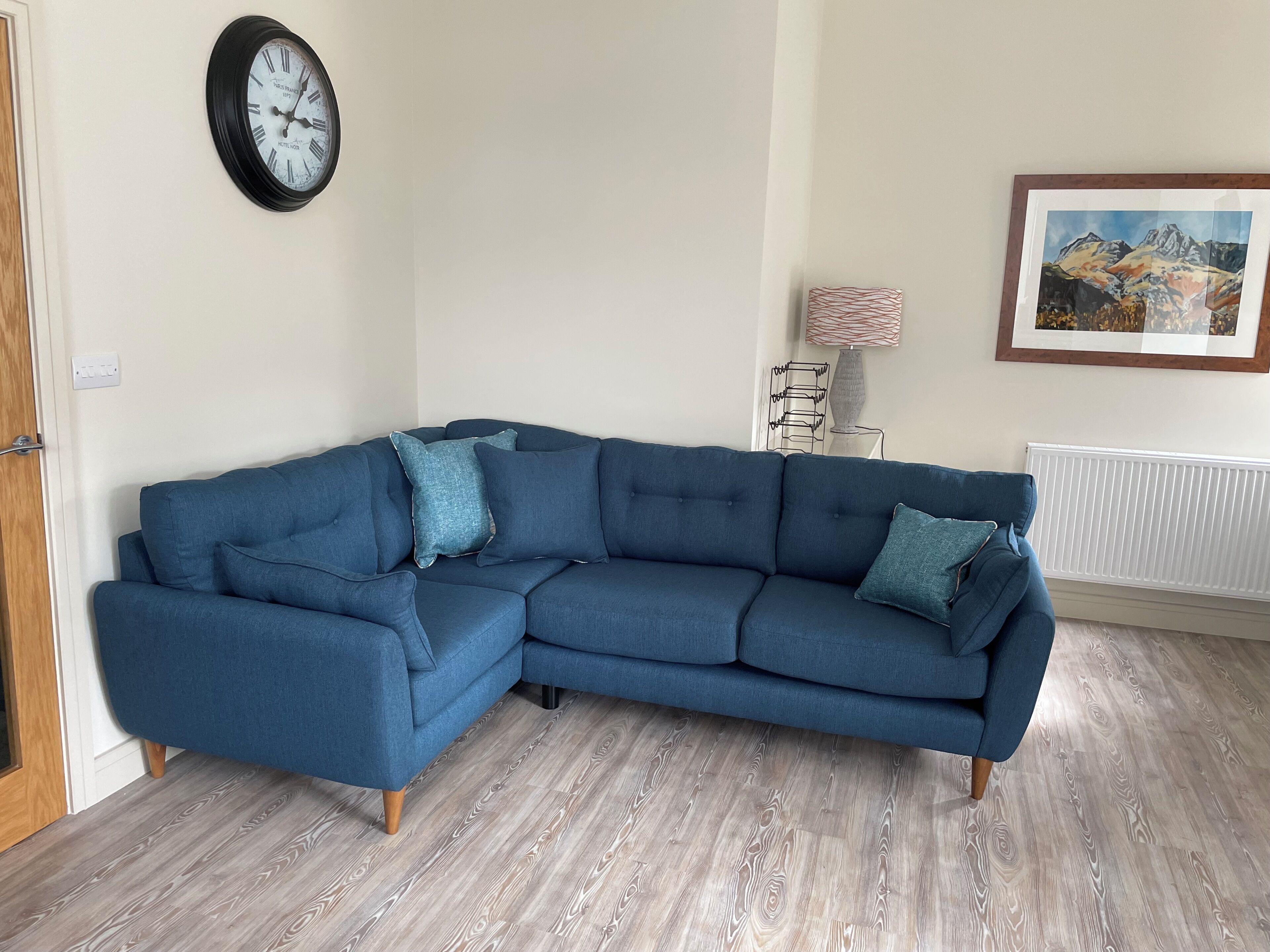 A corner sectional sofa with a clock and a framed landscape painting on the wall.