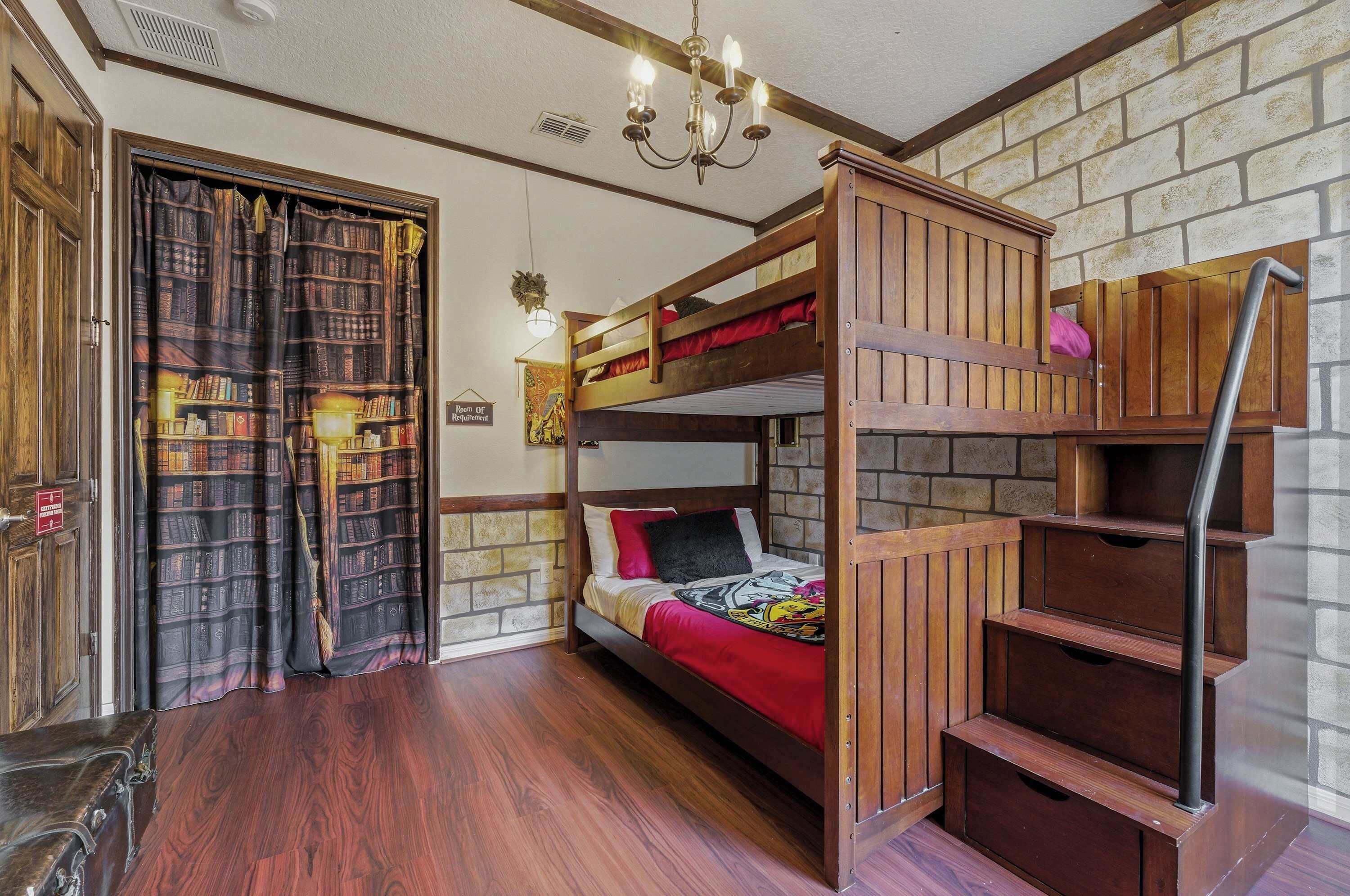 A bunk bed room with a wooden staircase, a chandelier, and a bookshelf curtain.