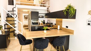 A modern kitchen with a wooden island, black chairs, and a staircase with a black railing. - Naturiste Cap d'Agde Villa Héliovillage 23 (Agde)