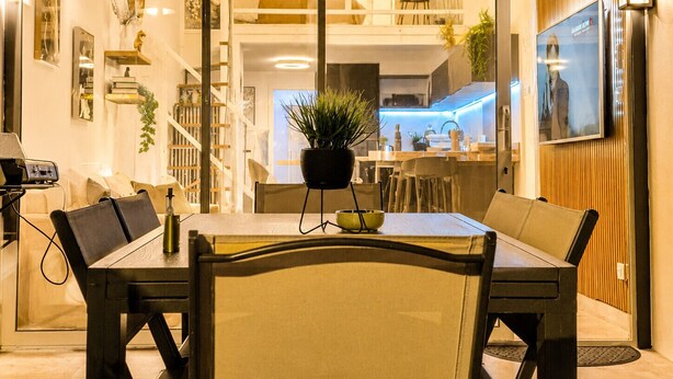 A modern dining area with a table, chairs, a potted plant, and a kitchen in the background. - Naturiste Cap d'Agde Villa Héliovillage 23 (Agde)